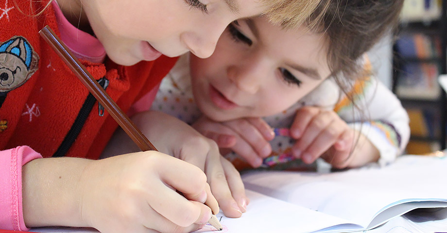 Två barn i en skolbänk som skriver i ett block