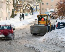 En plog i ett tättbebyggt område med både en bil och gående på trottoar