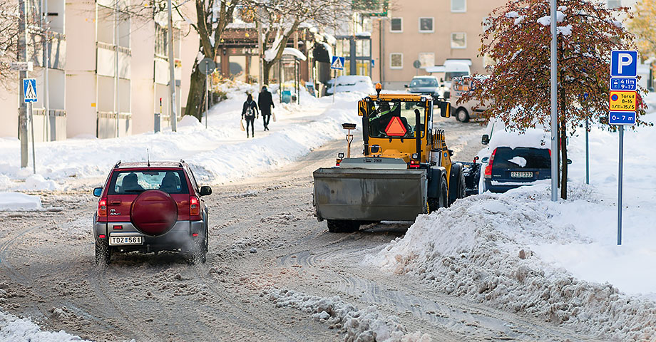 En plog i ett tättbebyggt område med både en bil och gående på trottoar