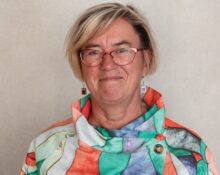 Porträtt av kvinna med glasögon, ljust hår i pagefrisyr och färgglad blus.