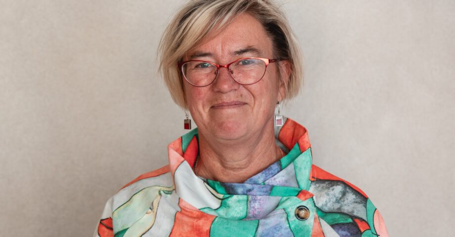 Porträtt av kvinna med glasögon, ljust hår i pagefrisyr och färgglad blus.